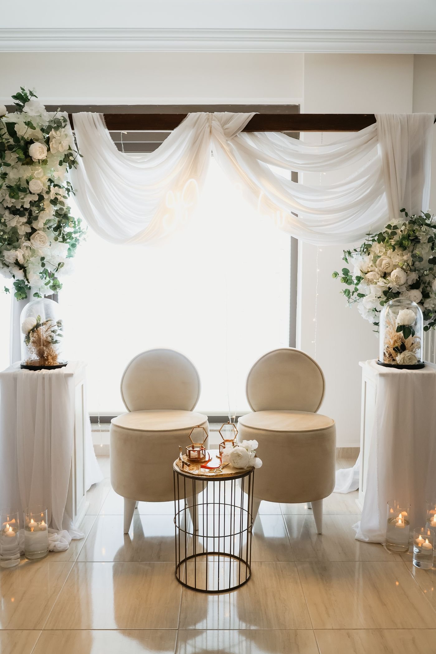 Twee stoelen met wit doek, kaarsen en bloemen, opgesteld voor een nikah ceremonie